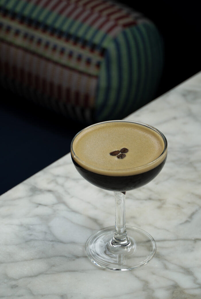 Espresso martini served in a coupe glass on a marble tabletop, garnished with three coffee beans.