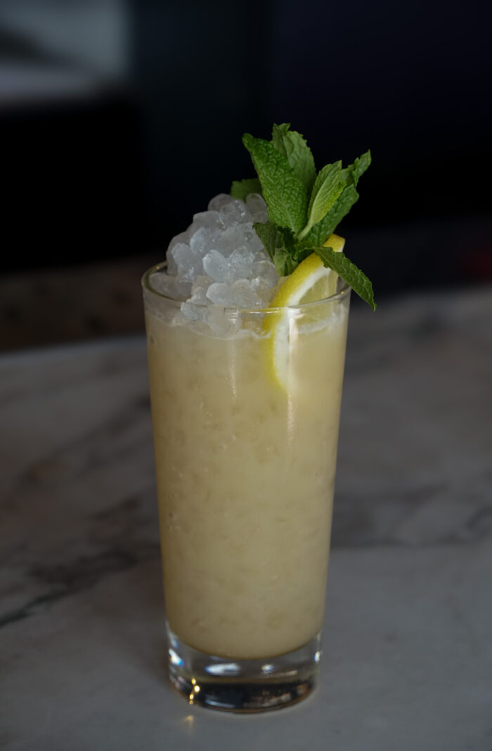 Creamy cocktail in a tall glass filled with crushed ice, garnished with a lemon wedge and fresh mint.