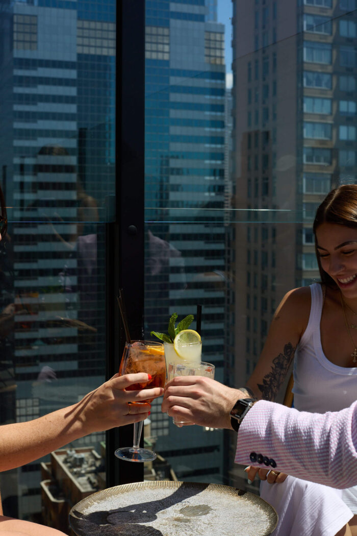Group toasting cocktails at a rooftop table with city skyline in background.