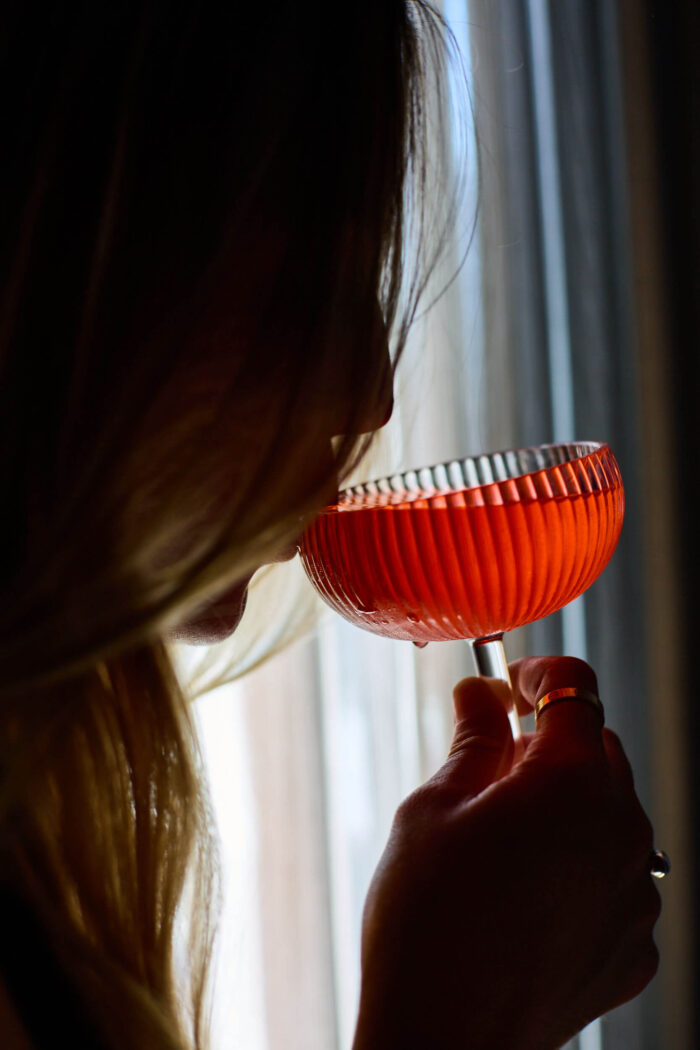 Woman sipping a red cocktail in natural light near window.