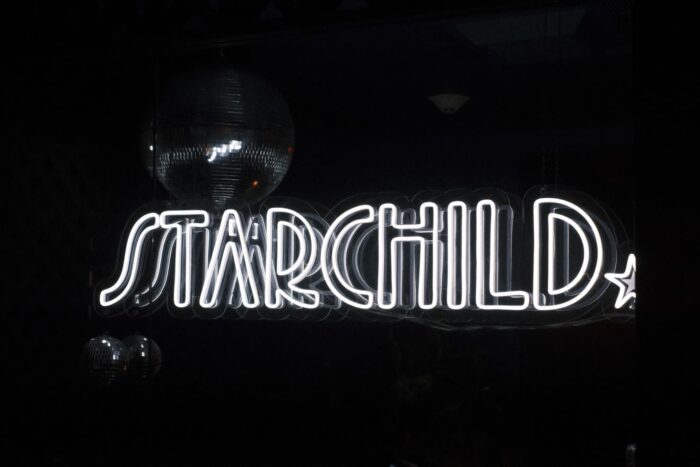 Glowing neon STARCHILD sign with disco ball overhead in a dark venue