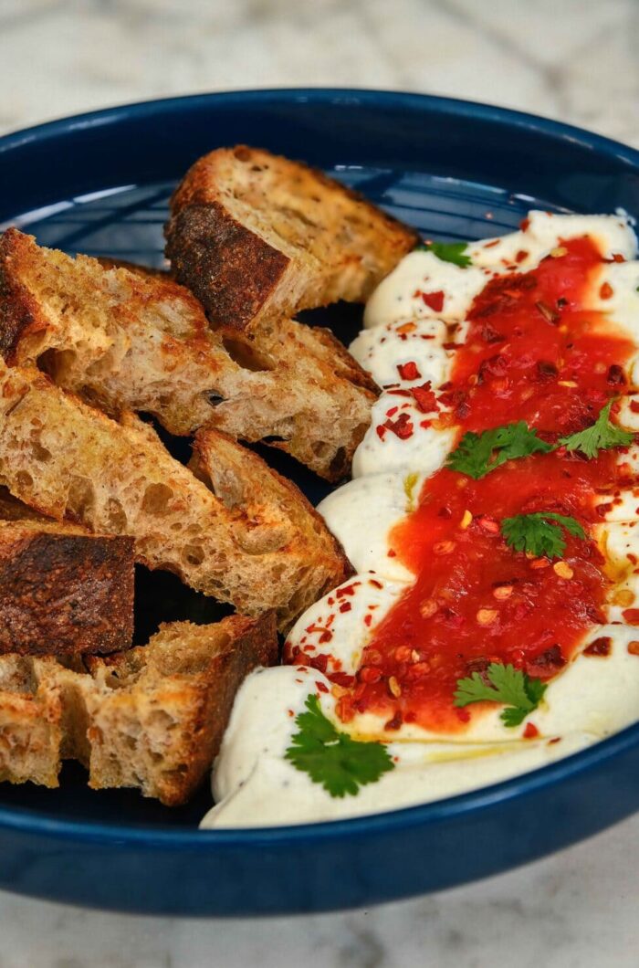 Grilled artisan bread served with whipped dip topped with tomato spread and herbs