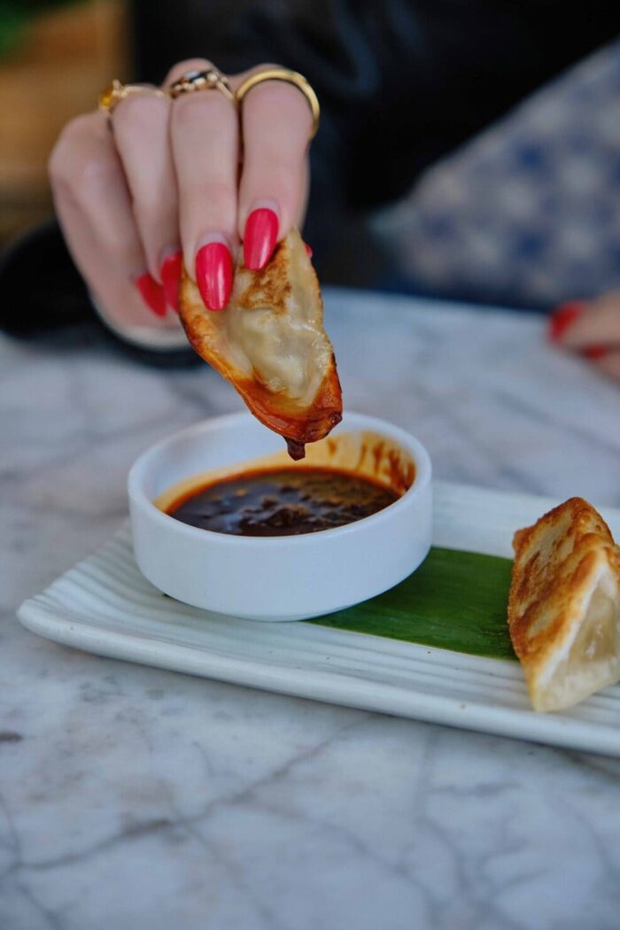 Close-up of a crispy dumpling being dipped into soy sauce in a white bowl on marble table.