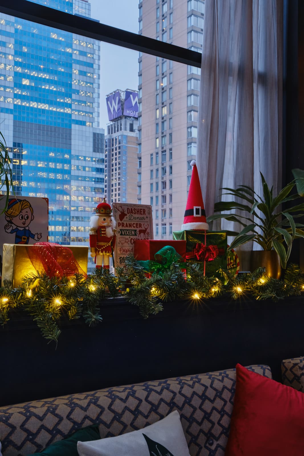 Festive Christmas display at StarChild Rooftop featuring wrapped gifts, a nutcracker, a Santa hat, and illuminated garlands beside a large window overlooking city buildings.
